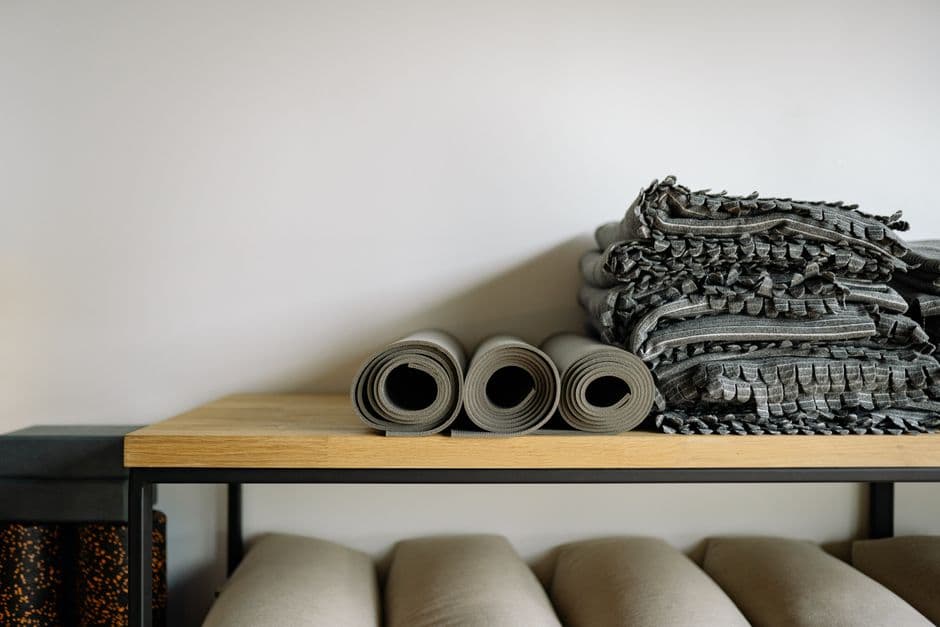 Tapis de yoga roulés et couvertures pliées sur un banc de bois dans une salle claire