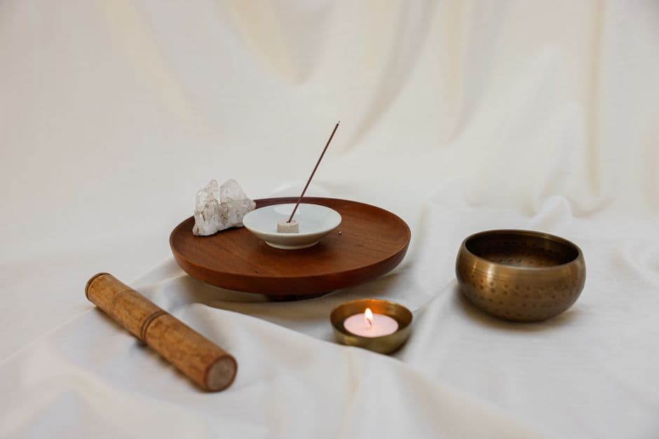 Bol chantant, bâton d'encens et bougie posés sur un plateau en bois, lumière douce